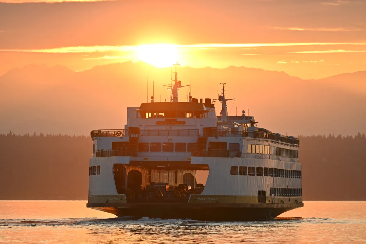 The Washington State ferry Walla Walla approaches, the setting sun just above its mast and the Olympic Mountains behind.